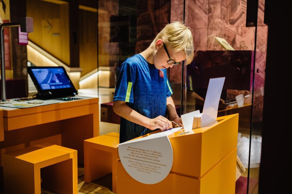 Ein junger Besucher beugt sich über eine Familienspur in der Dauerausstellung 