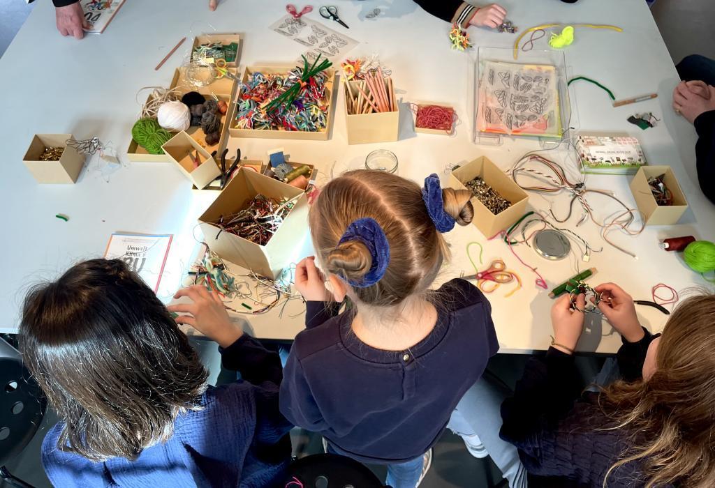 Der Schrott-Basteltisch in der Ausstellung Blick von oben, Kinder beugen sich über einen Tisch mit Bastelmaterialien.