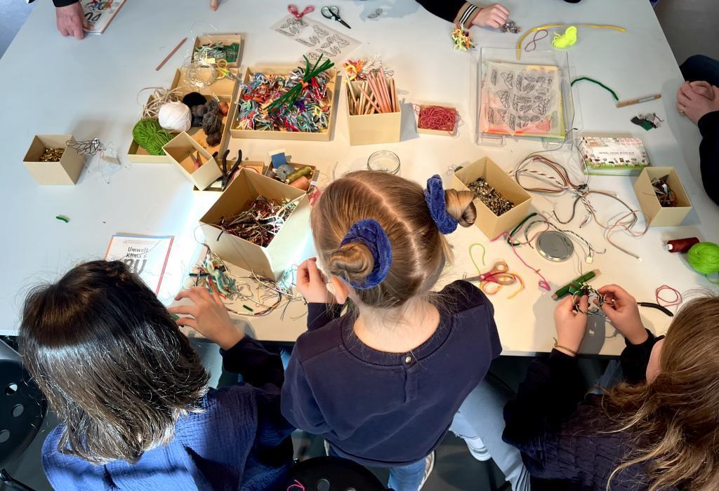 Blick von oben, Kinder beugen sich über einen Tisch mit Bastelmaterialien.