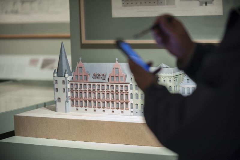 Ein Foto zeigt ein Modell des Museums und eine Person, die etwas in ihr Smartphone tippt