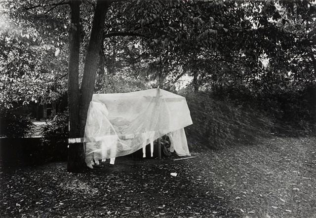 Das Schwarz-Weiß-Foto von Abisag Tüllmann zeigt ein Plastikplanenzelt von Obdachlosen in einem Park.
