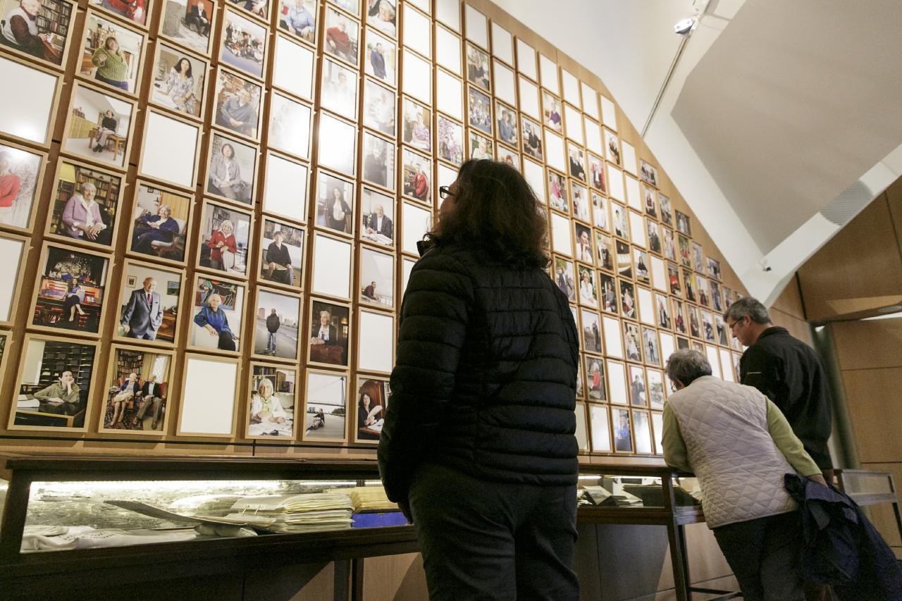Ein Foto zeigt Besucher*innen vor einer Bilderwand mit Fotos von den Autor*innen der Bibliothek der Generationen.