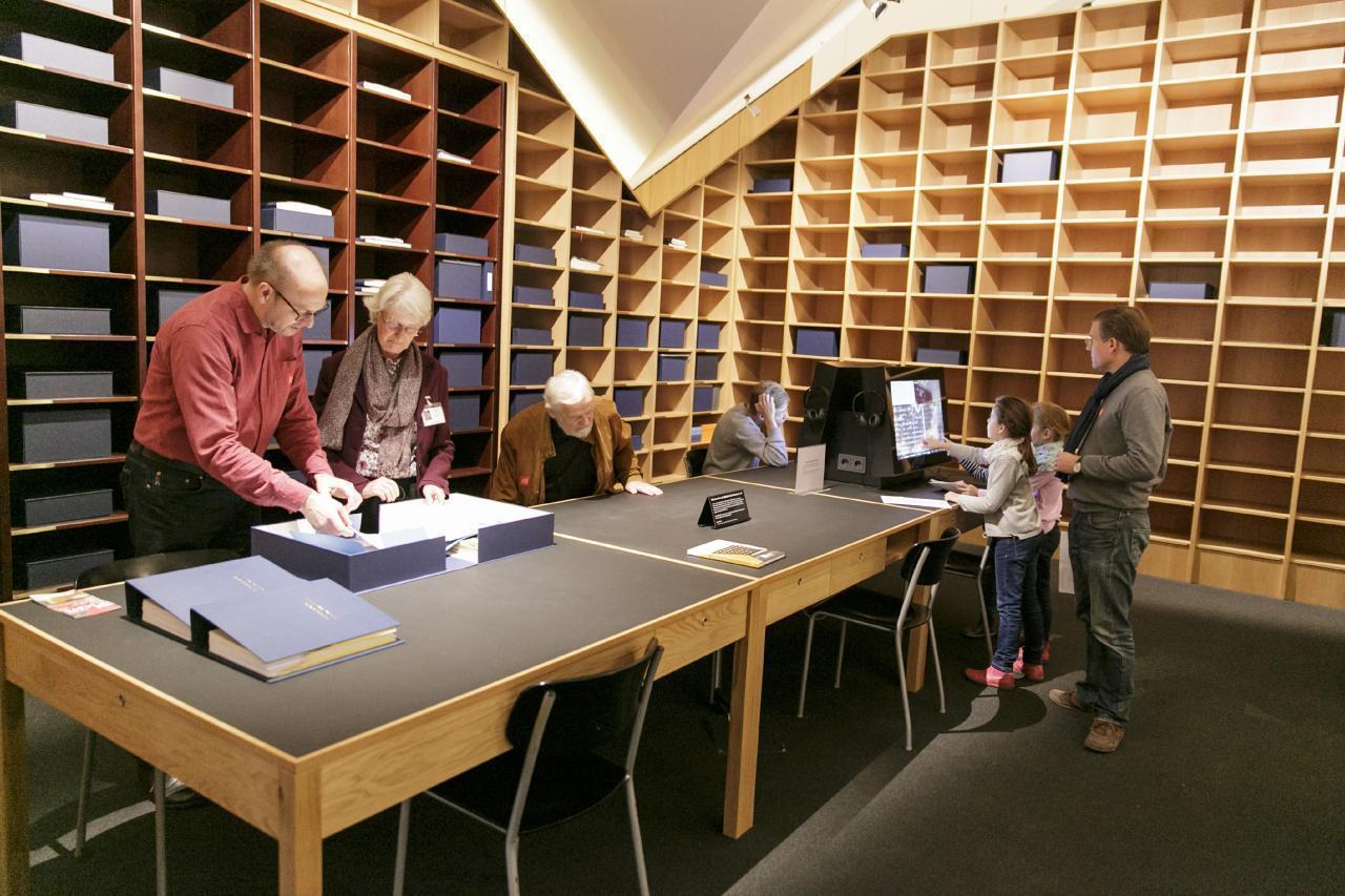 Ein Foto zeigt Besucher*innen in der Bibliothek der Generationen, die in einer Kassette einen Beitrag anschauen und an der Medienstation recherchieren.