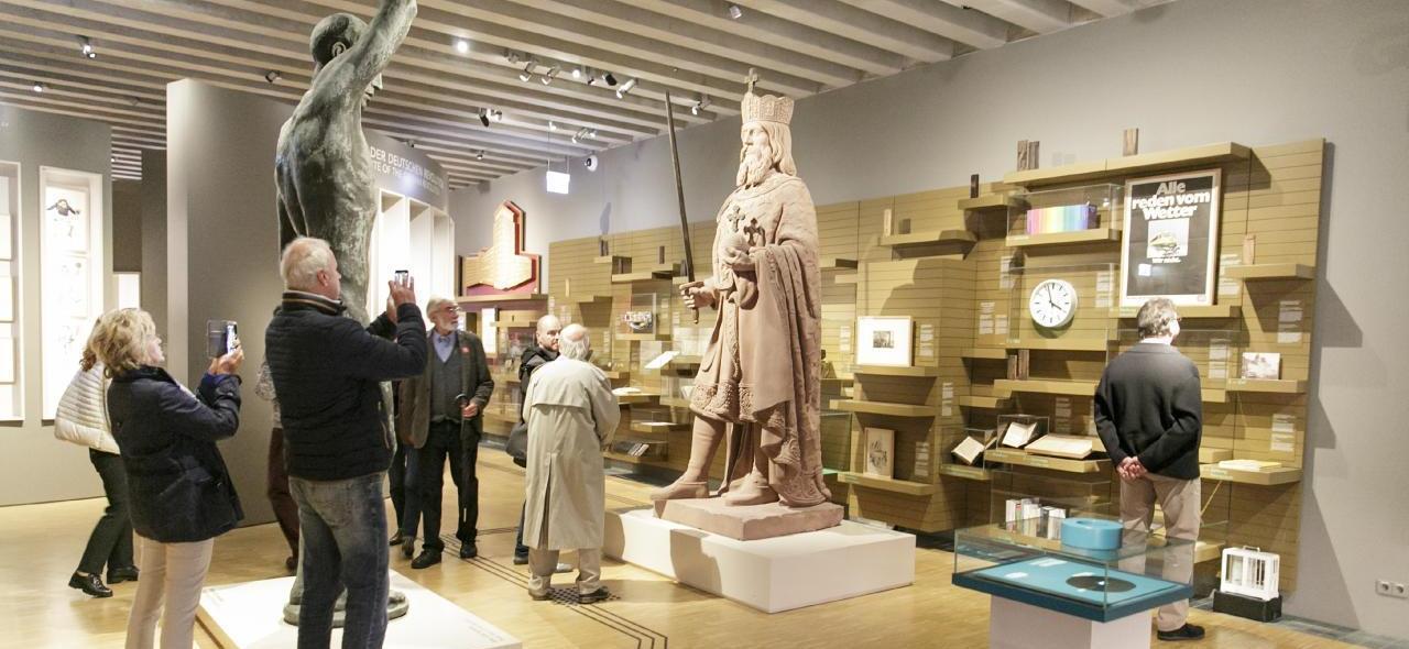 Auf dem Bild sind Besucher/innen im Museum zu sehen, die Fotos von der Statue Kaiser Karls machen