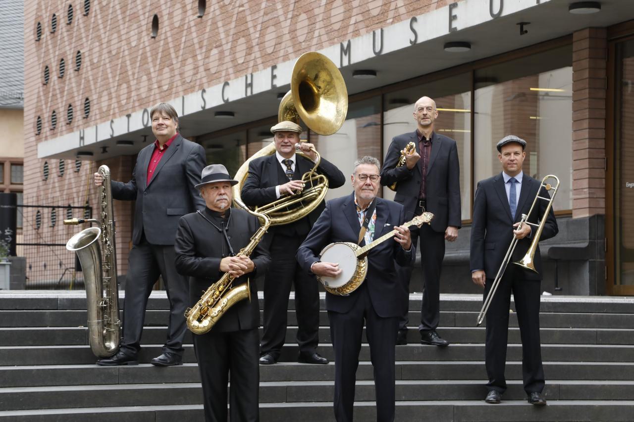 Das Foto zeigt sechs Mitglieder der HMF-Allstars auf den Stufen vor dem Museumseingang. Alle tragen ihre Instrumente in der Hand.