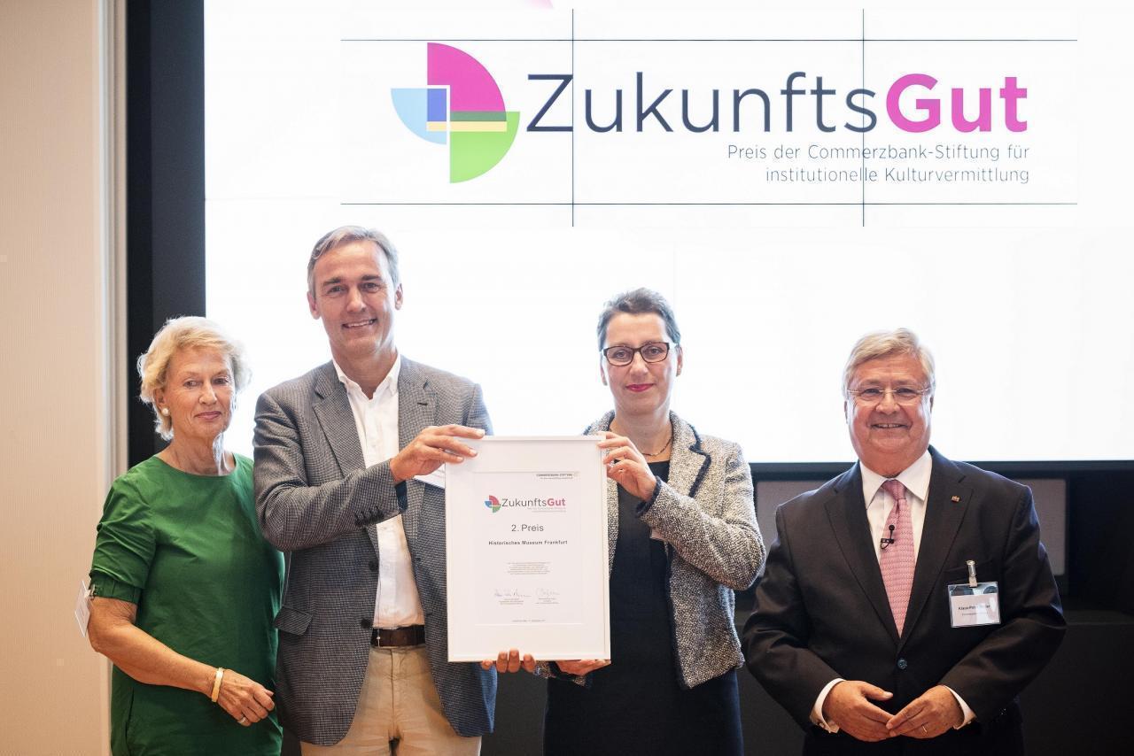 Das Foto zeigt vier Personen, in der Mitte Herr Gerchow und Frau Gesser, die das Zertifikat für den 2. Preis halten. 