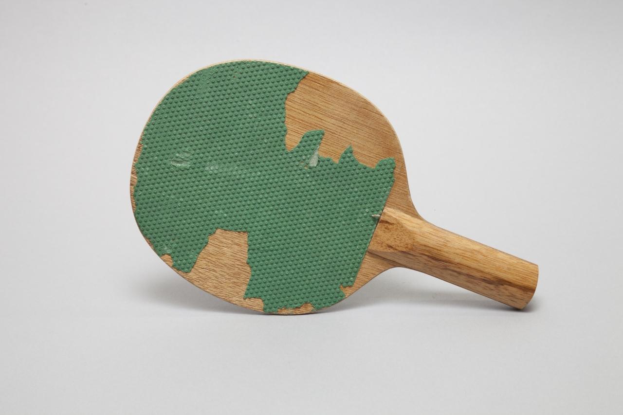 Das Foto zeigt einen Tischtennisschläger aus Holz mit beschädigtem grünem Gummibezug.
